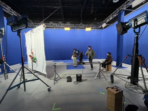 Virtual production stage with blue screen, cinema camera on dolly track, lighting, and crew