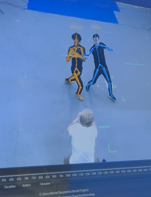 Markerless motion capture session: two performers with live skeletal tracking overlaid, viewed on a studio monitor with capture software UI