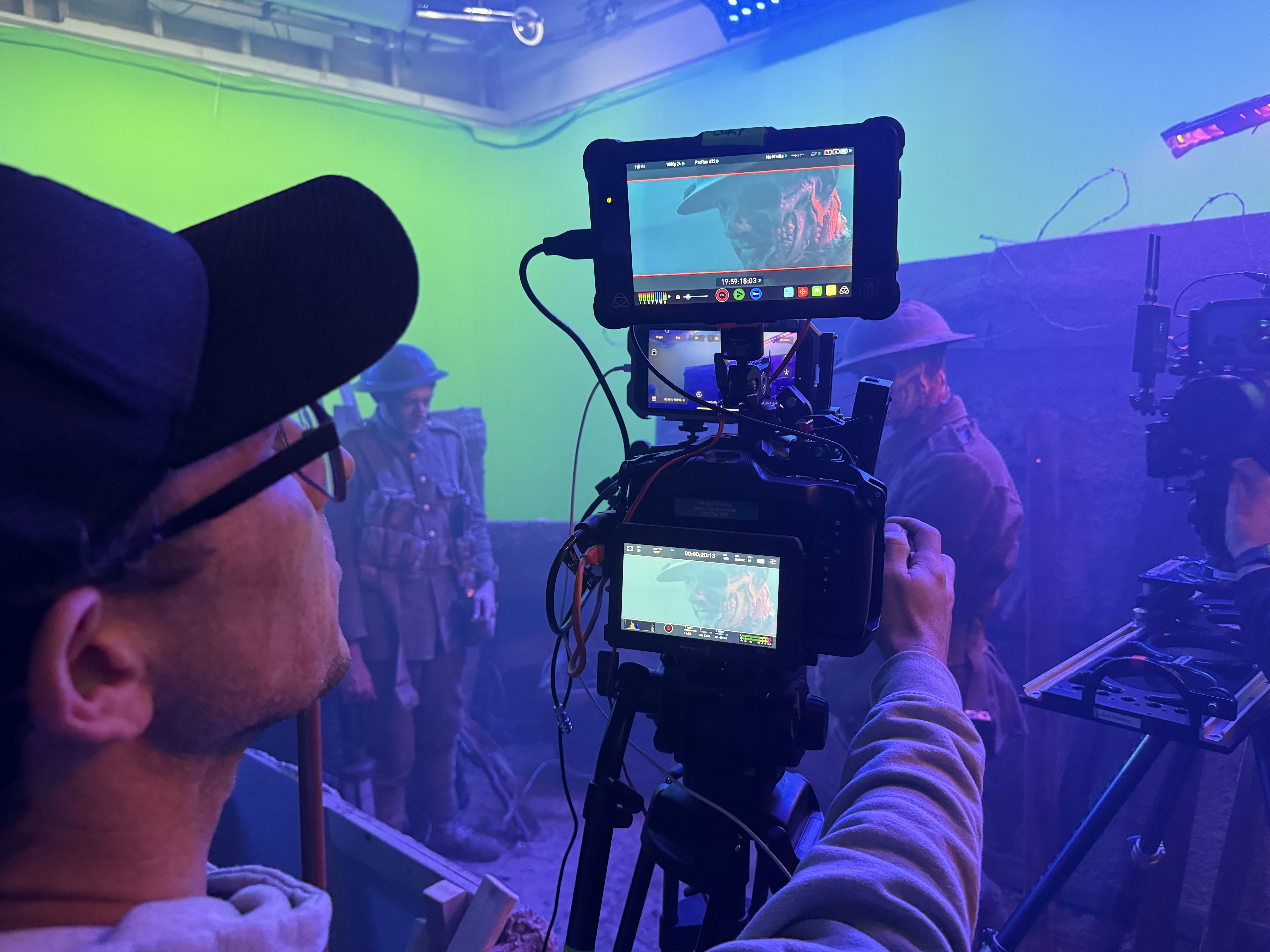 Virtual production set: cinema camera and monitors with performers in period costume against green screen and atmospheric lighting